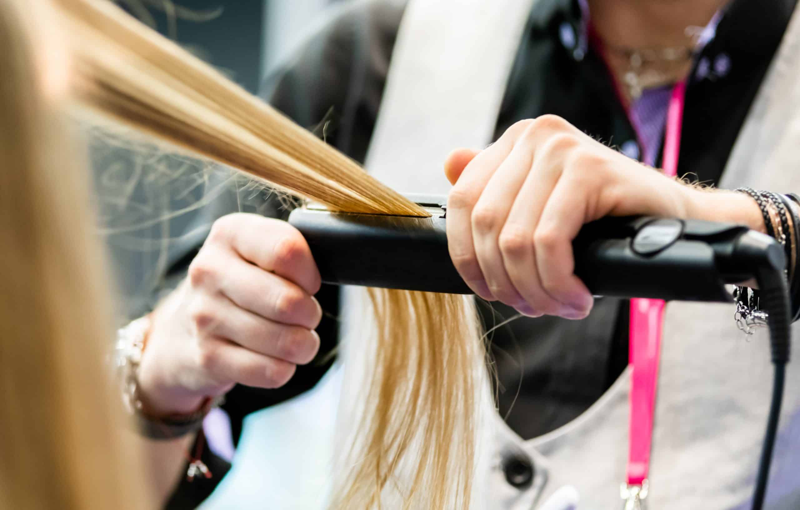 Professional hairdresser straightening long blond hair using straightener